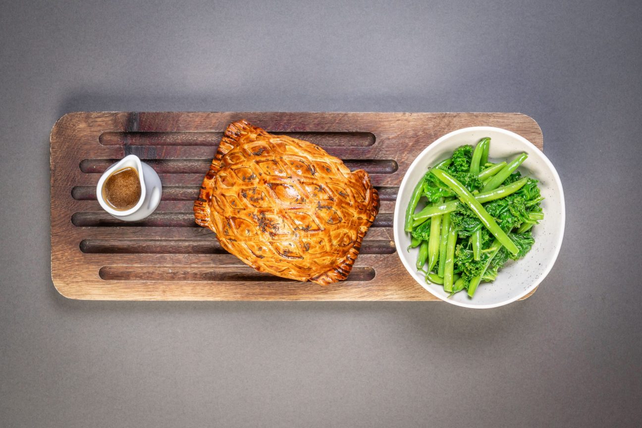 perfect beef wellington with greens and gravy on a serving board